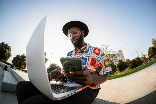 Black man multitasking using laptop and smartphone outdoors