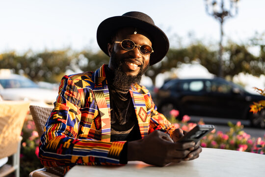 Stylish man smiling wearing African print jacket using phone