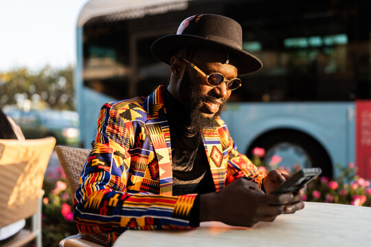 Black man wearing kente pattern blazer using phone at cafe