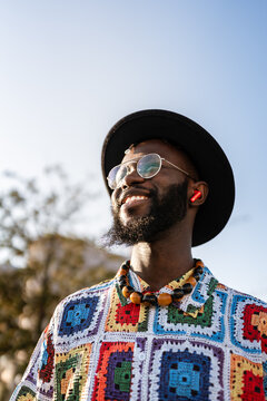 Smiling man wearing colorful crochet shirt and wireless earbuds