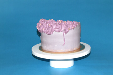 A beautiful cream cake stands on a stand against a blue background. A very delicious cake.