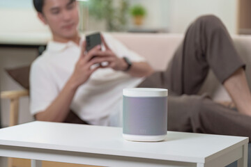 Technology and Lifestyle. Young man using smartphone while relaxing with smart speaker at home.