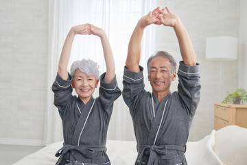 寝室で伸びをするシニア夫婦　カメラ目線
