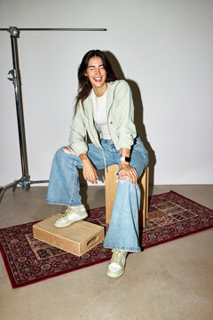 Smiling woman in casual outfit sitting on wooden box