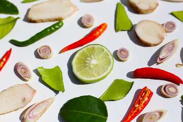 A colorful, close-up pattern of Thai herbs: lime slices, galangal, lemongrass, chilies, and kaffir lime leaves.