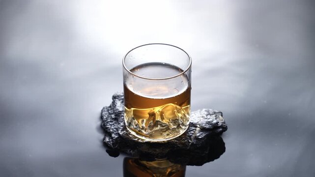 Glass of whiskey on volcanic rock with water reflection and dramatic cloudy sky background