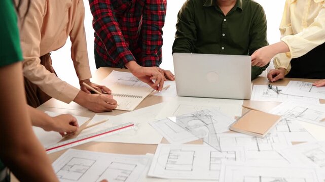 Architect and safety engineer discussion about building blueprint displaying on laptop on table with architectural document and wooden block scatter around at modern office. Closeup. Delineation.