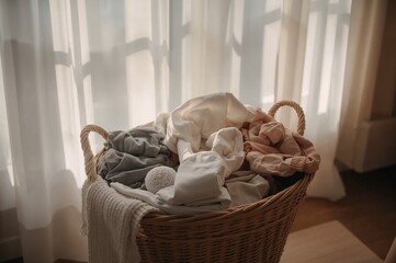 Sunlight-Drenched Laundry Basket Overflowing with Soft Textiles Near Sheer Curtains.