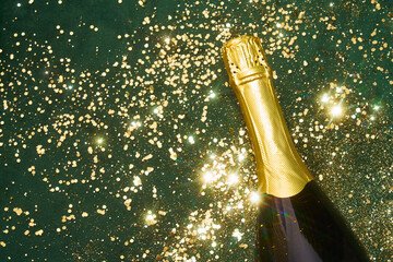 Champagne bottle on green surface with golden glitter