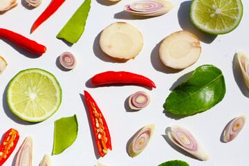 A colorful, close-up pattern of Thai herbs: lime slices, galangal, lemongrass, chilies, and kaffir...