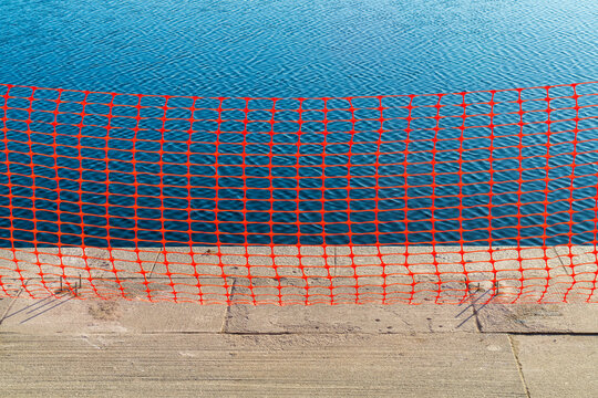 Red plastic barrier in front of blue water
