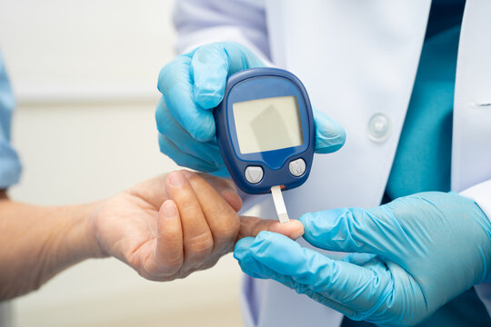 Asian doctor using digital glucose meter for check sample blood sugar level to treatment diabetes.