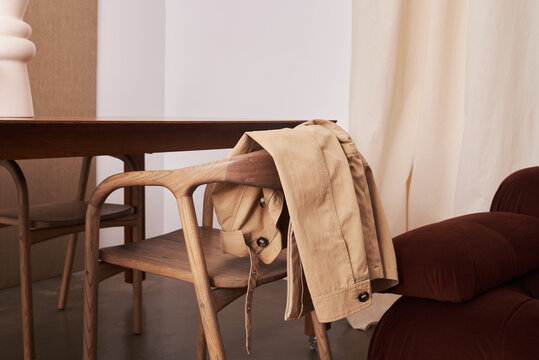 Beige jacket draped over a wooden chair in a minimalist interior - Powered by Adobe