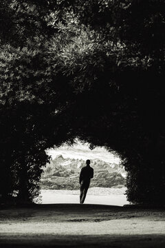 Solitary Figure Walking Through a Natural Arch by the Water