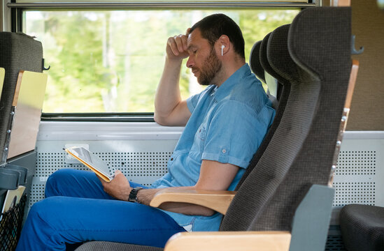 Person Reading Quietly on a Train, using a tablet and earbuds