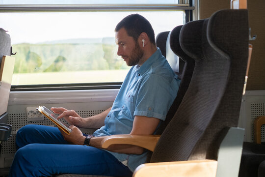Man Reading on a Train using a tablet and earbuds