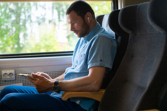 Man Enjoying a Train Ride While Using a Tablet and earbuds 