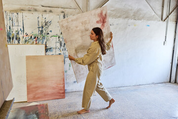 Woman carrying large canvas in art studio during creative sessio