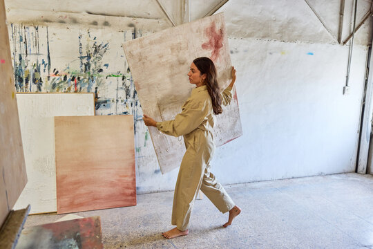 Woman carrying large canvas in art studio during creative sessio