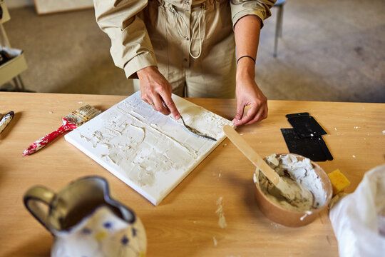 Artist creates textured artwork using white paint and tools