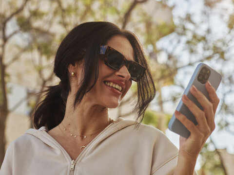 Woman Smiling While Using a Smartphone Outdoors in the Sunlight