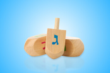 Three wooden dreidels with Hebrew letters resting against blue