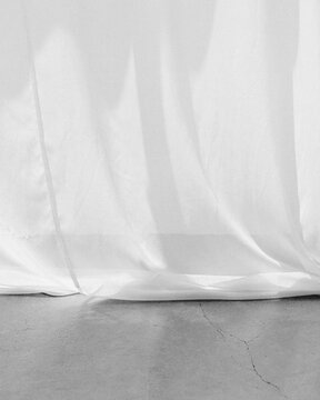 White curtain touching cracked concrete floor in sunlight
