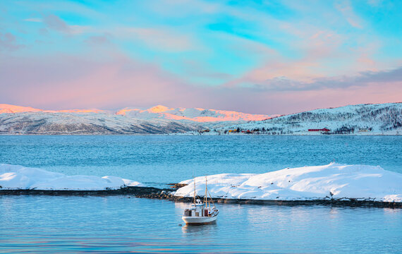 Fisher shelter in winter with fishboat at sunset in the background snowy mountains and Norwegian fjords - Tromso, Norway