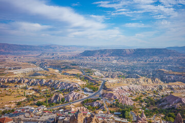 A wide panoramic view of Cappadocia’s breathtaking valley in Turkey, showcasing layered rock formations, pastel-colored ridges, and dramatic geological textures stretching toward the distant mountains