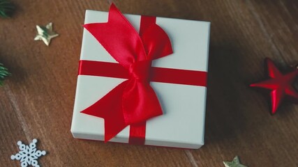 White present box with red ribbon bow and festive ornaments on wooden table background.