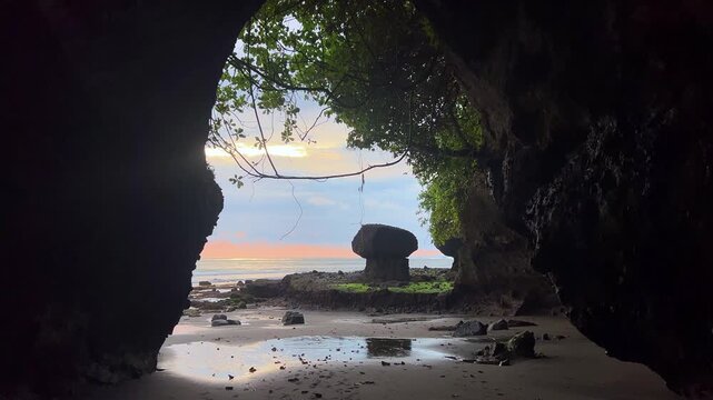 Beautiful sunset near a natural cave on Soan Galuh Beach in Tabanan. A beach with black volcanic sand and bizarre mushroom-shaped rocks on the island of Bali, Indonesia. 4К
