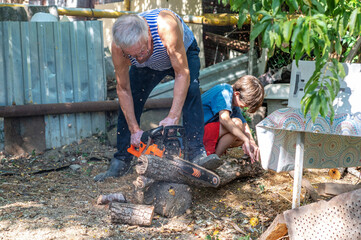 Grandfather teaching grandson how to cut wood with a chainsaw outdoors