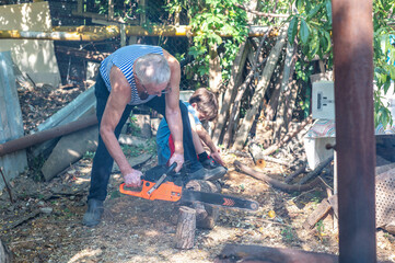 Grandfather teaching grandson how to cut wood with a chainsaw outdoors