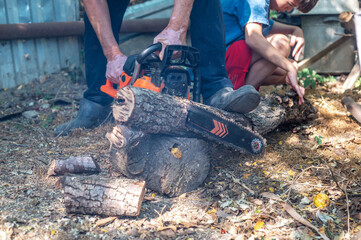 Grandfather teaching grandson how to cut wood with a chainsaw outdoors