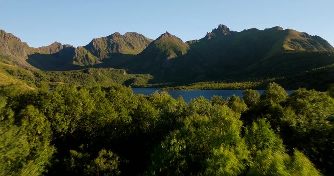 Drone video flying over dense green forest to reveal a scenic lake surrounded by mountains at Teigvatnet near Stokmarknes in northern Norway, showcasing peaceful Nordic nature