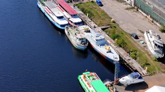 Aerial View of a Busy Riverside or Canal Dockyard Featuring Various Moored Vessels, from Brightly Colored Passenger Ships and Workboats to Smaller Yachts, on a Sunny Day in an Urban Industrial Setting
