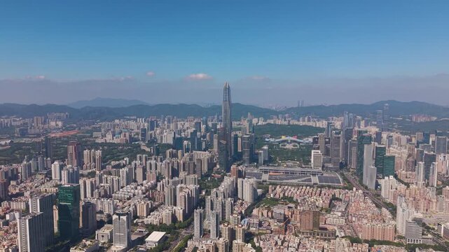 Wide drone shot of Shenzhen&rsquo;s skyline featuring Ping An Finance Centre rising above dense urban districts. Modern high-rises, green park areas, and distant mountains under a clear blue sky. China.