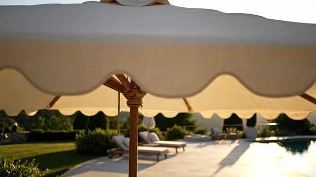 Underneath a canvas parasol, a luxury pool area with loungers and landscaping basks in soft golden light