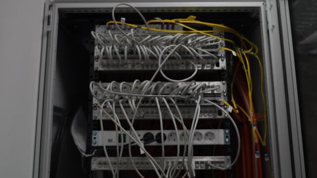 Network cable cabinet with multiple patch panels and bundled wiring inside a technical equipment rack. White and yellow cables visible in an electrical or communication setup.