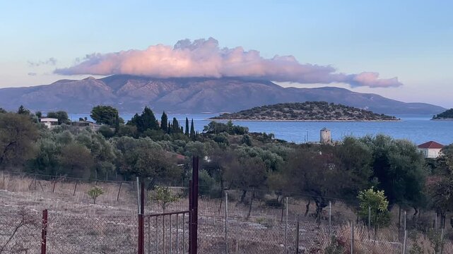 Kalamos Island and Mytikas,Still Frame,Footage from a country side towards the mountains covered with white pink clouds at mainland. Beautiful country side with olive trees,windmill.