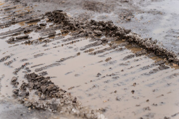 Deep construction vehicle tire tracks filled with water on a muddy worksite ground, showing heavy-equipment movement patterns, wet terrain conditions, and industrial site surface wear