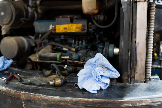 Engine repair area featuring exposed mechanical parts, detached sensor element, blue workshop towel, and maintenance tools arranged on equipment body during technical servicing operation