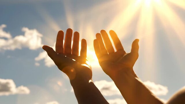 Two hands raised upwards against a bright, sun-drenched sky with fluffy clouds, creating a serene and hopeful image