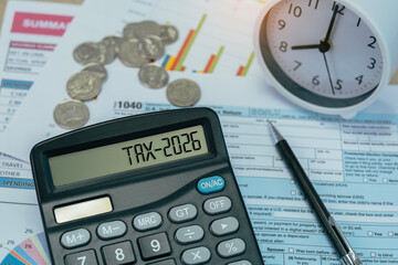 Word Tax 2026 on the calculator on documents. Income Statement. income tax form, coins, and financial documents on wooden desk, symbolizing budgeting, filing, and fiscal strategy