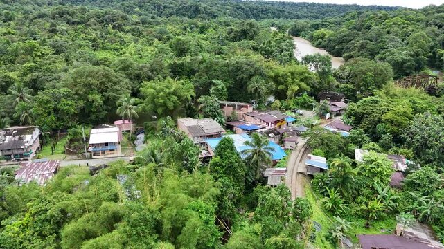 Aerial follows the disused railway track over a rustic iron bridge crossing the muddy river in San Cipriano, Colombia, surrounded by dense jungle