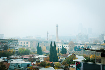 Autumn cityscape of Tbilisi under heavy smog, showing a contrast between old and modern buildings with hazy skyline and muted colors, evoking urban melancholy and environmental concern