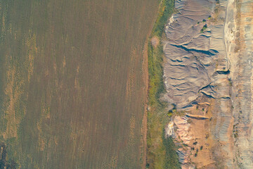 Stark vertical contrast in land use seen from a drone: a uniform agricultural field meets a severely eroded, complex geological formation with intricate patterns and sloping ridges.