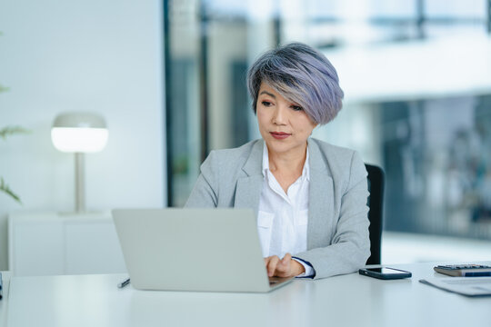 Asian senior businesswoman typing on laptop in office room