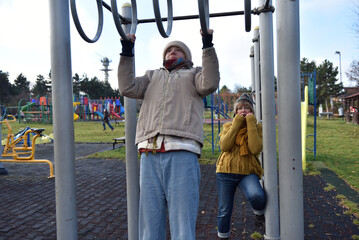 Teenager daughter and mother using gymnastic rings in outdoor gym park
