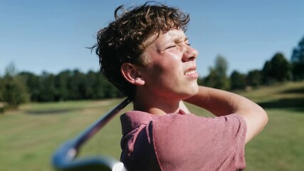 Teen golfer finishes swing under bright blue sky squinting into sunlight on green fairway capturing focus practice and healthy outdoor sports lifestyle - Powered by Adobe